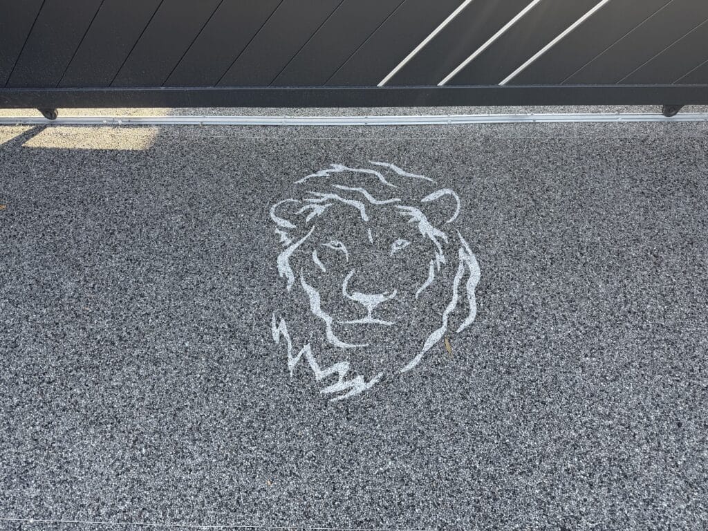 Dessin de tête de lion blanche sur sol en gravier noir près d'un portail métallique moderne.